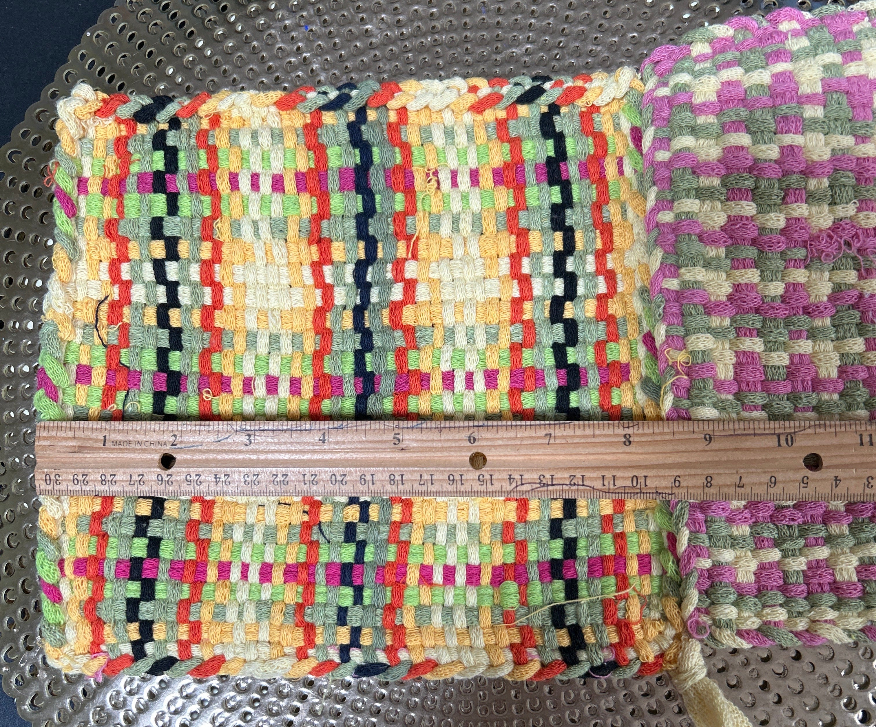 Multicolored woven mat with a ruler for scale on a textured surface